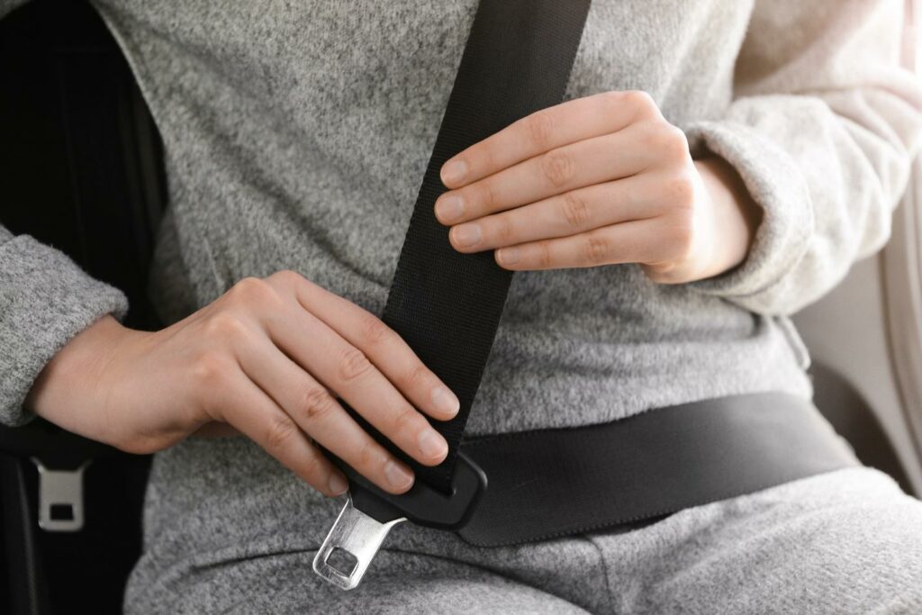 A woman dressed in casual gray clothing fastening her seatbelt.