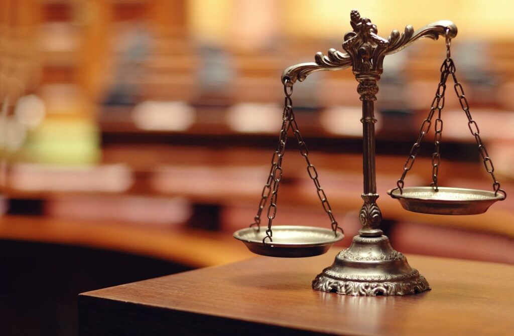 Concept photo of the scales of justice resting on a stand in a blurred courtroom.