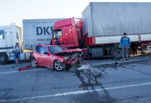A red semi-truck and a red two-door car in the aftermath of a head-on collision.