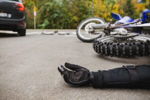 Injured motorcyclist lying in roadway next to fallen motorcycle behind a car pulled across the lane of traffic; motorcycle accident concept.