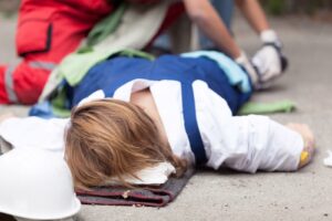 An injured worker lying on a folded blanket, receiving first aid treatment for a work site injury; workers’ comp concept.