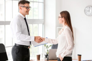 A personal injury lawyer greeting a client with a handshake in an office setting.