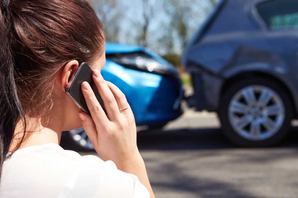 Distressed driver standing on roadside making phone call while looking at rear end collision car accident.