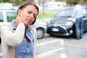 A woman winces in pain and holds her right hand against her neck, a common area for a pre-existing injury aggravated in a car accident.