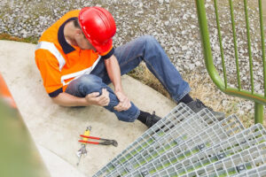 A construction worker holding his leg in pain at the base of some steps, wondering what damages are recoverable under workers’ compensation.