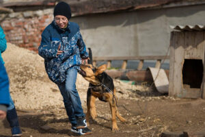 A child wearing jeans and a coat runs from a dog biting his coat. A dog bite can be particularly harmful to children.