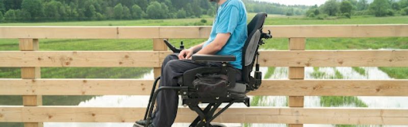 A young man in a wheelchair experiencing paralysis after a car accident, enjoys an nature outing on a boardwalk.