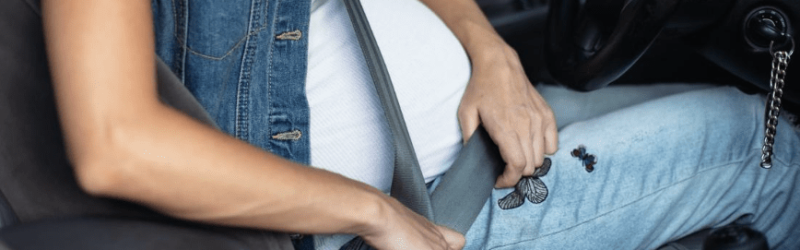 A pregnant driver adjusts her lap belt.