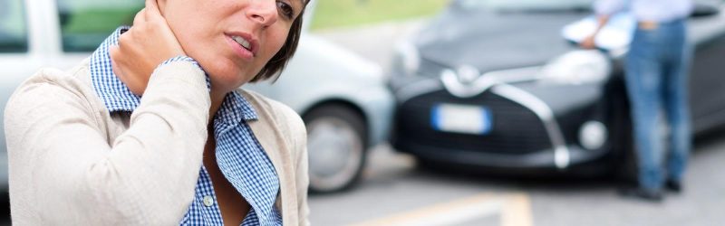 A woman winces in pain and holds her right hand against her neck, a common area for a pre-existing injury aggravated in a car accident.