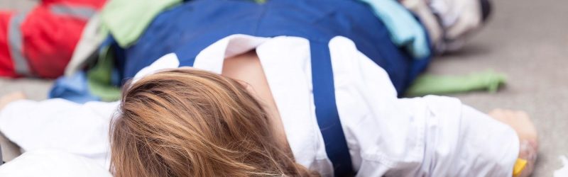 An injured worker lying on a folded blanket, receiving first aid treatment for a work site injury; workers’ comp concept.