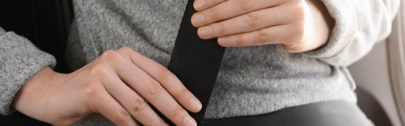 A woman dressed in casual gray clothing fastening her seatbelt.